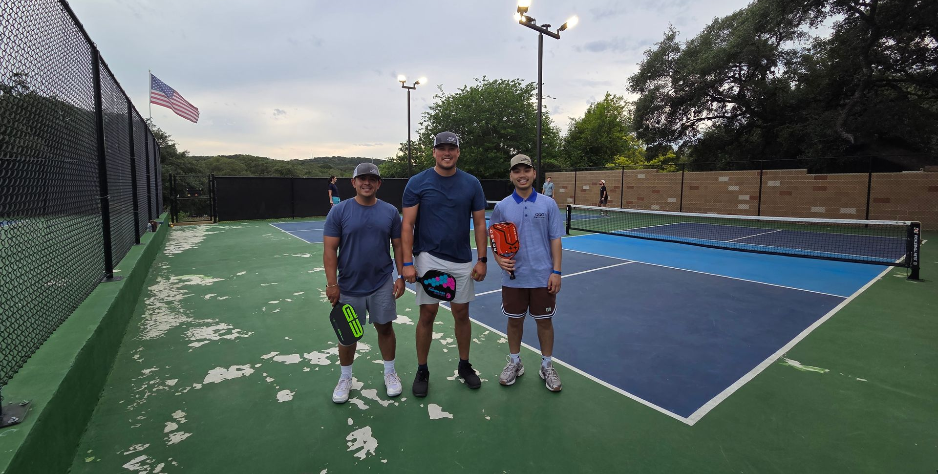 Three GGC employees standing on an outdoor pickleball court, holding rackets and facing the camera.