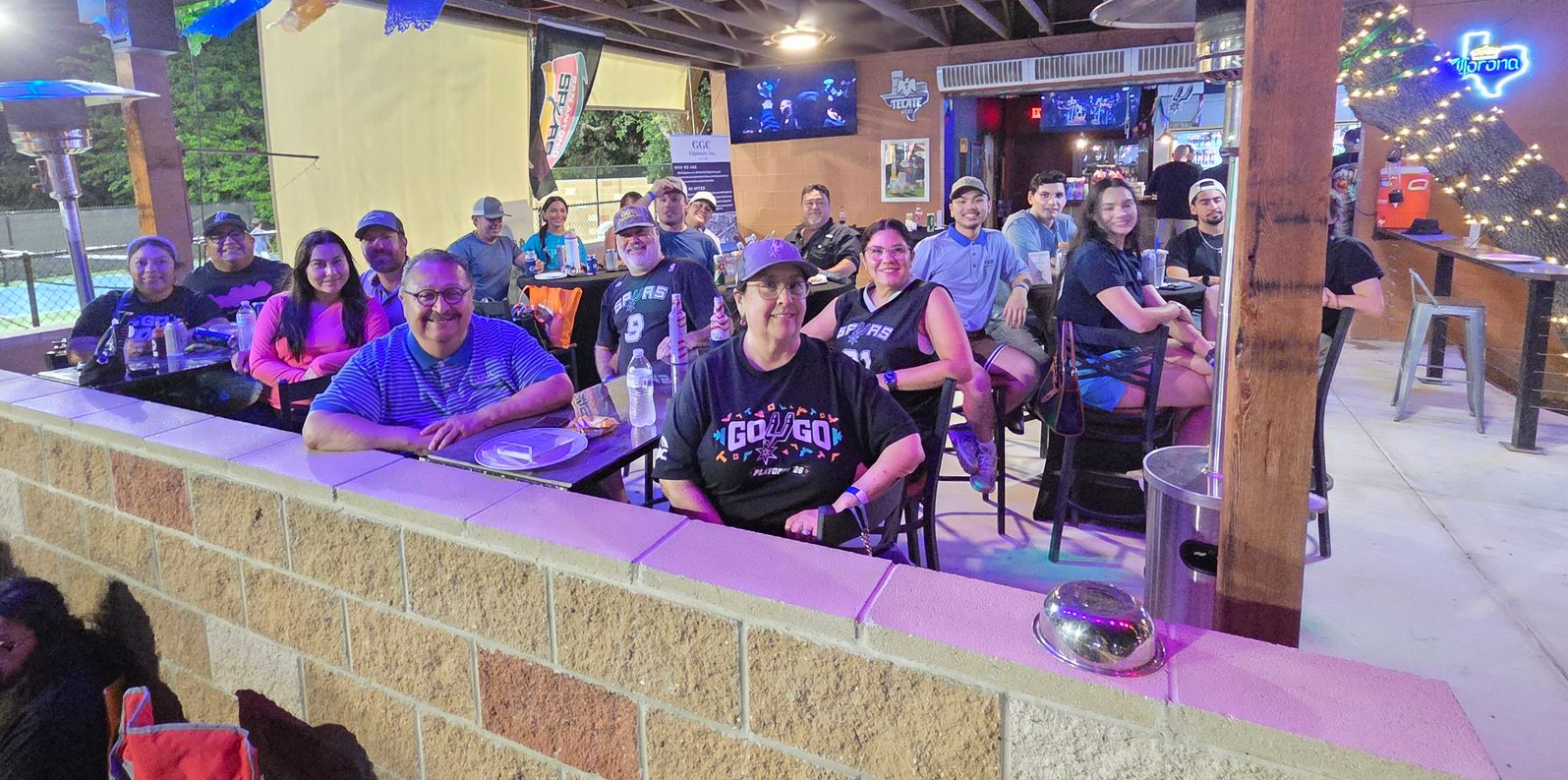GGC Engineers, Inc. team seated at a restaurant patio, smiling under colorful string lights at night