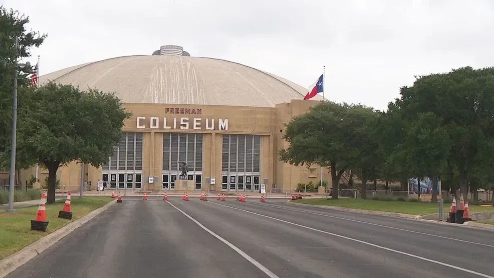 Front view of a large domed coliseum with a road leading to its entrance and trees on both sides