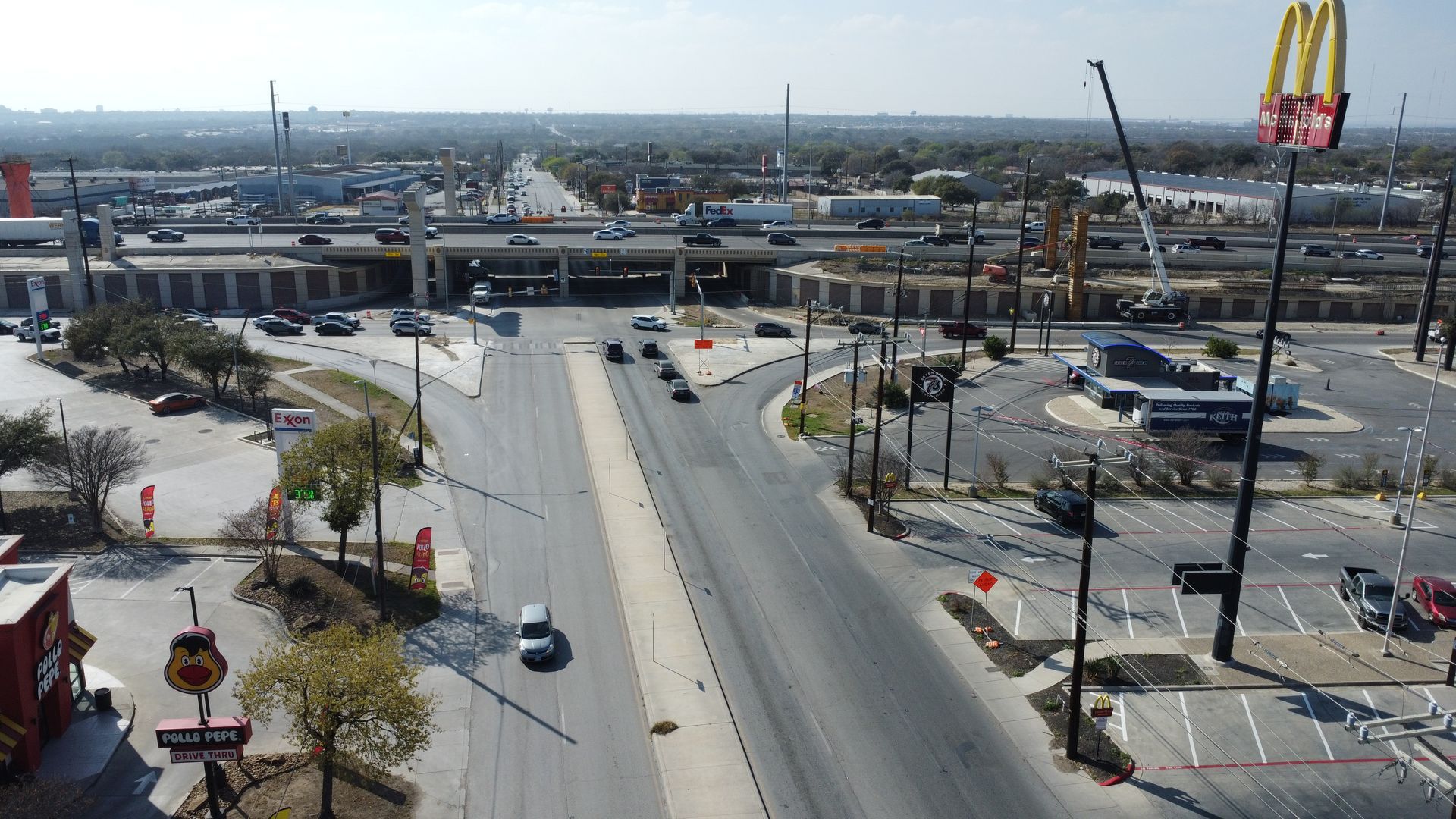 Wide road leading to a busy  highway interchange with cars, overpass, and a commercial area.
