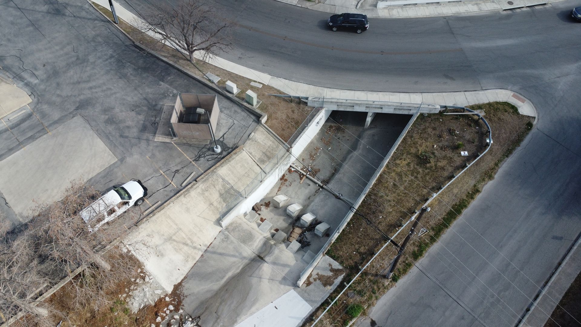 Aerial view of a concrete drainage culvert under a road, with a parked white car nearby.