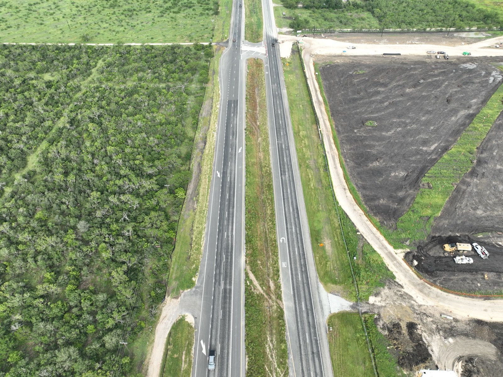 Aerial view of a highway cutting through green fields and dark plowed land prepared for construction.