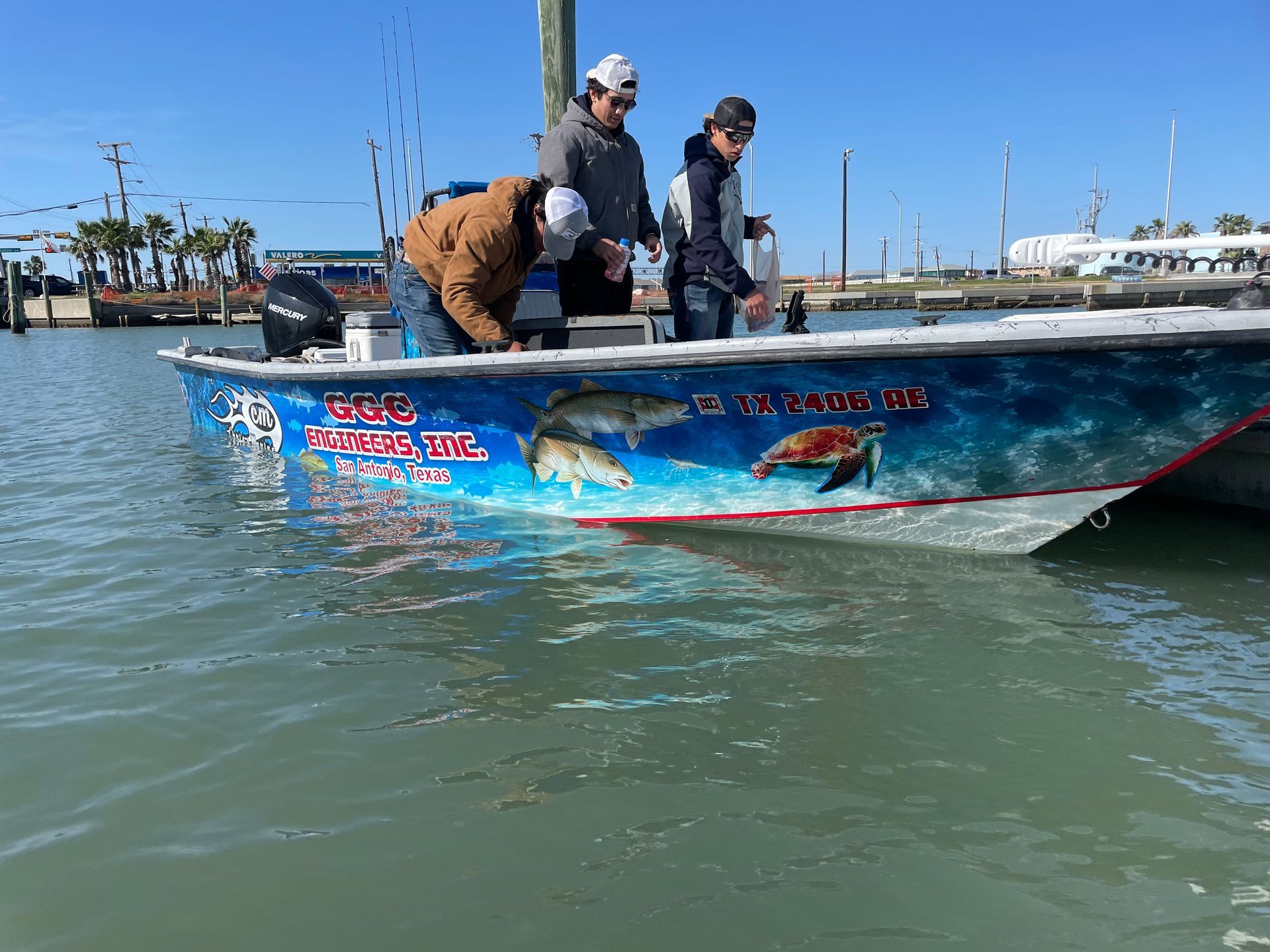 Two people on a blue GGC Engineers, Inc. fishing boat with in a marina.