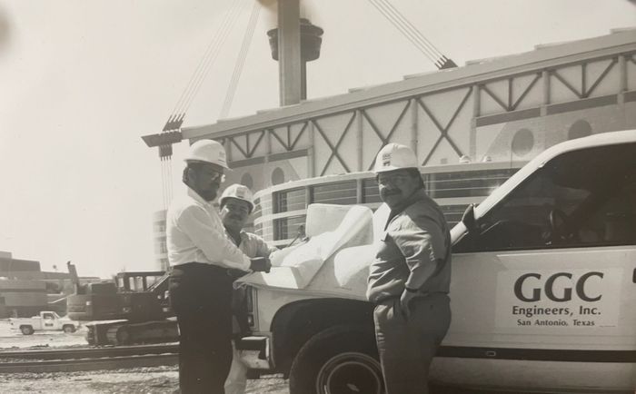 Three workers in hard hats standing by a white GGC service truck at the Alamodome during construction.