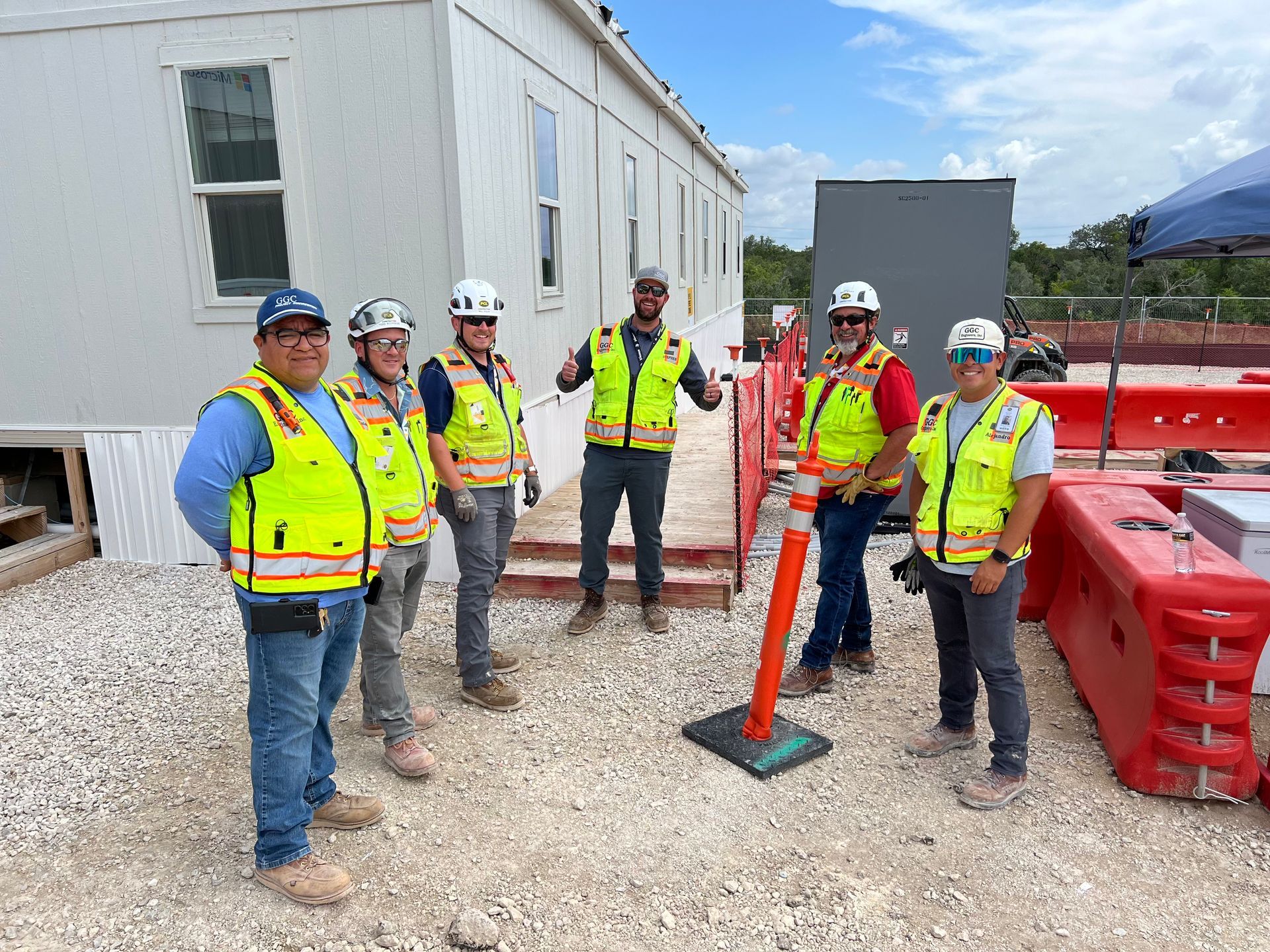 GGC Engineers, Inc. construction crew in neon safety vests and hard hats standing by a building site with red barriers.