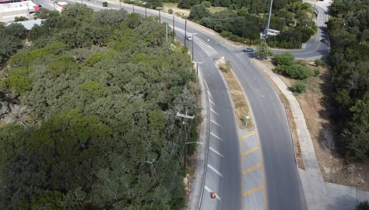 Road curving through a wooded area; trees line both sides with a car driving in the distance.