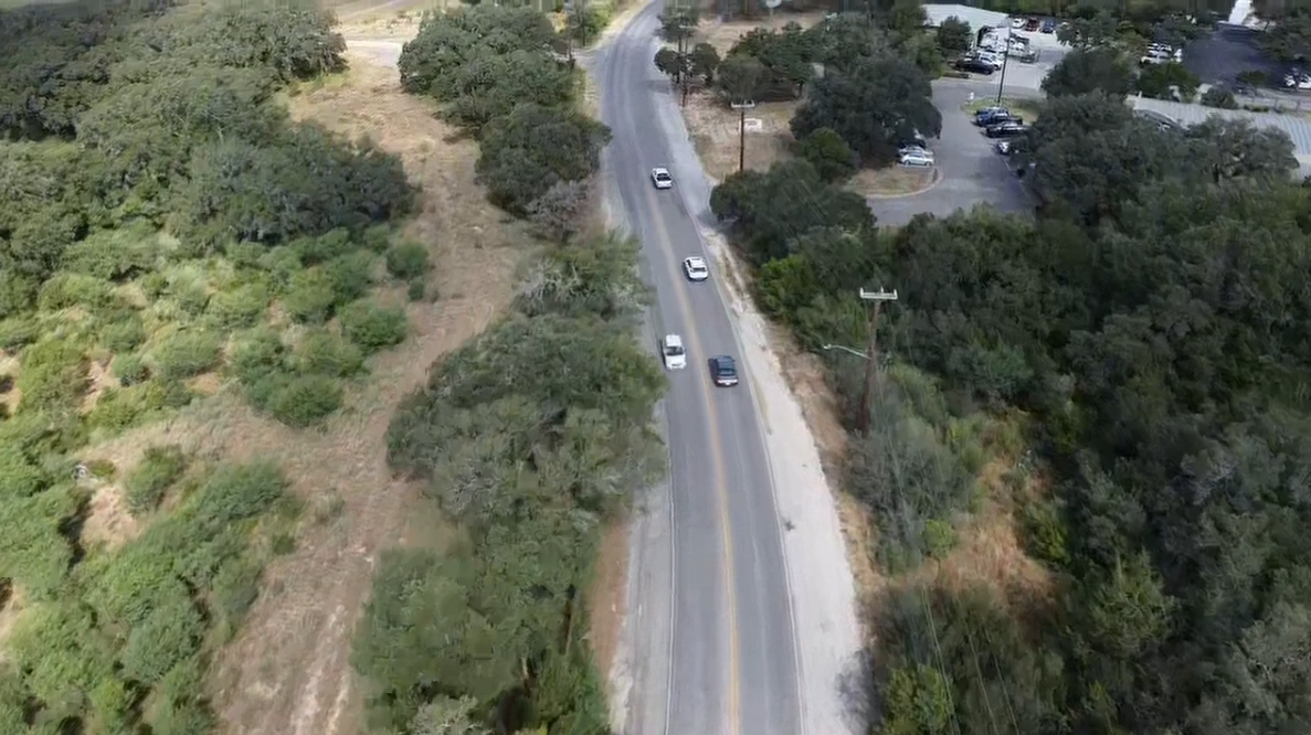 Aerial view of a two-lane road with cars, trees on both sides, and a building on the right.