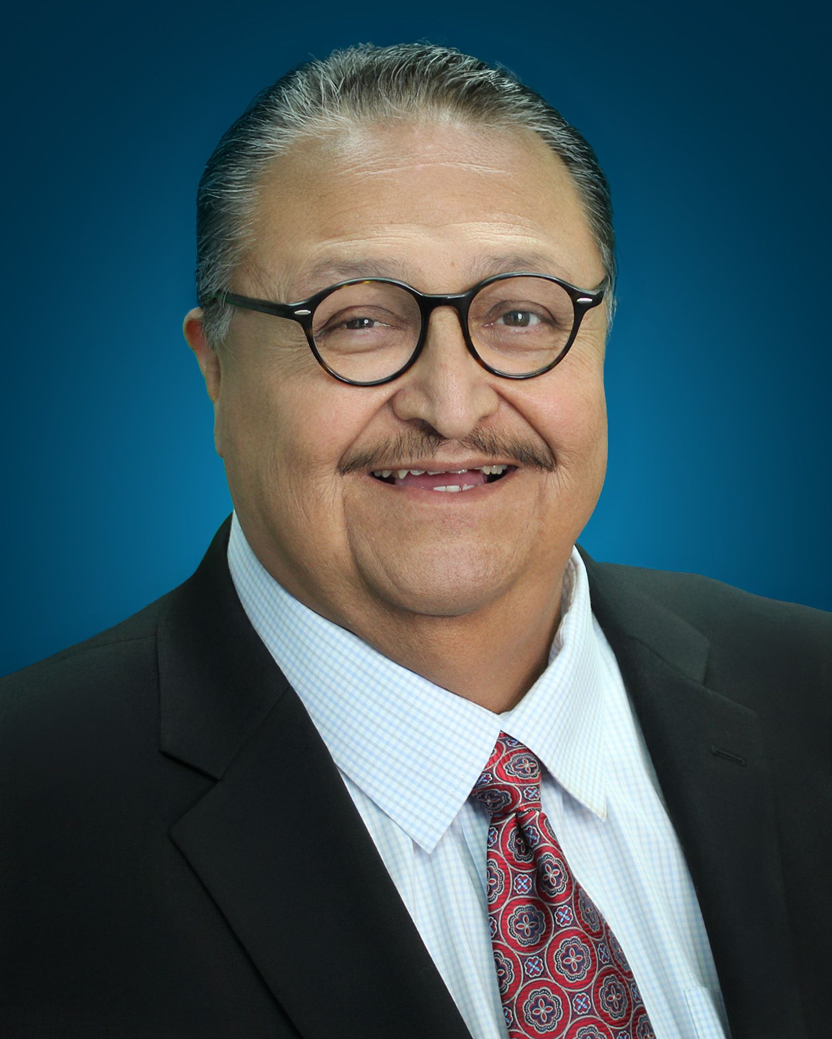 Headshot of Roberto P. González President/CEO smiling in a black suit against a blue gradient background.