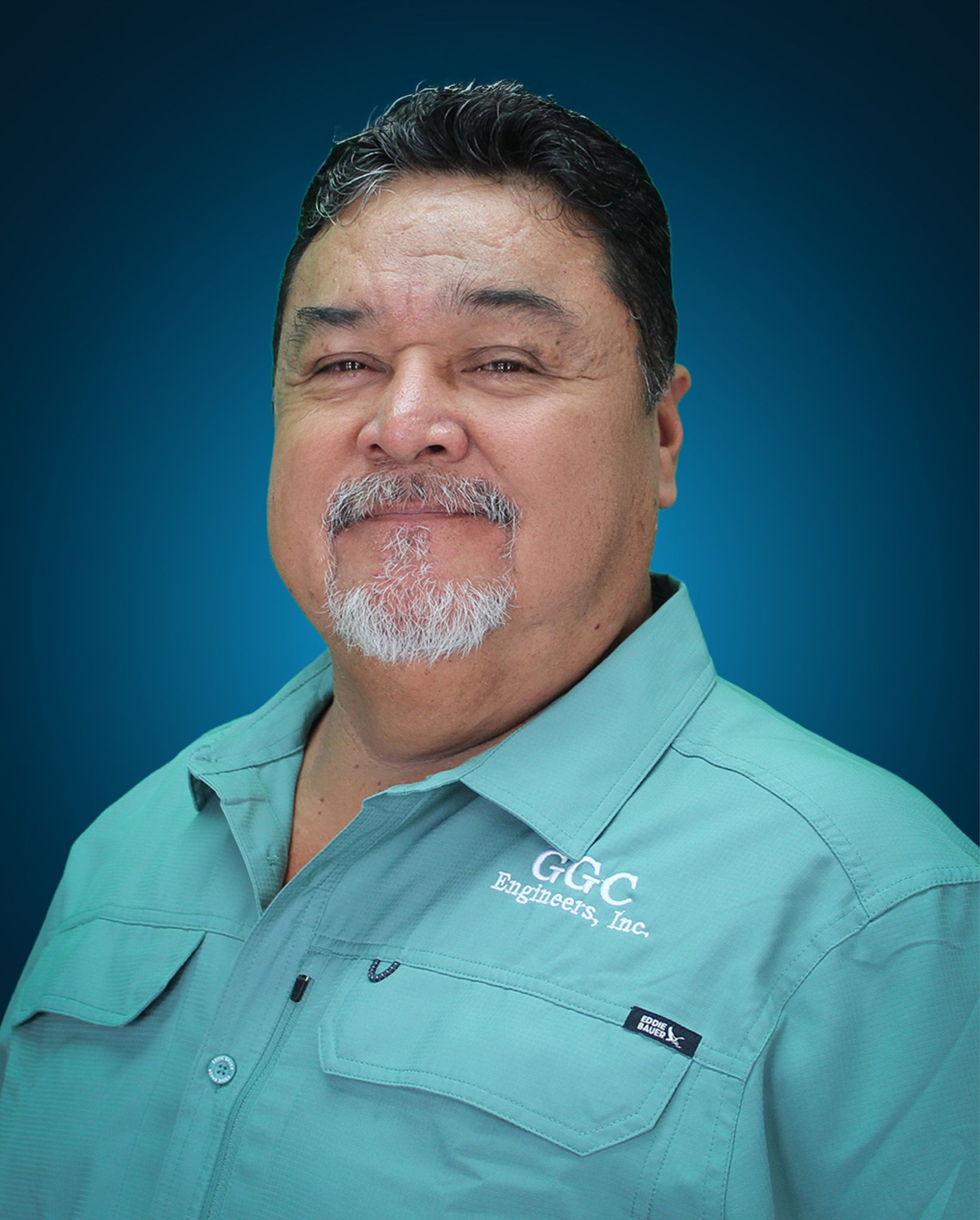 Man in teal shirt with goatee smiles, blue background. 