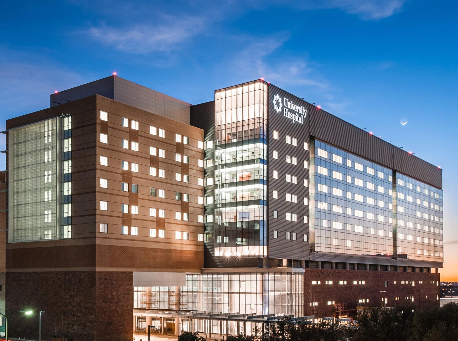 Hospital building at dusk with illuminated windows and a glass entrance.