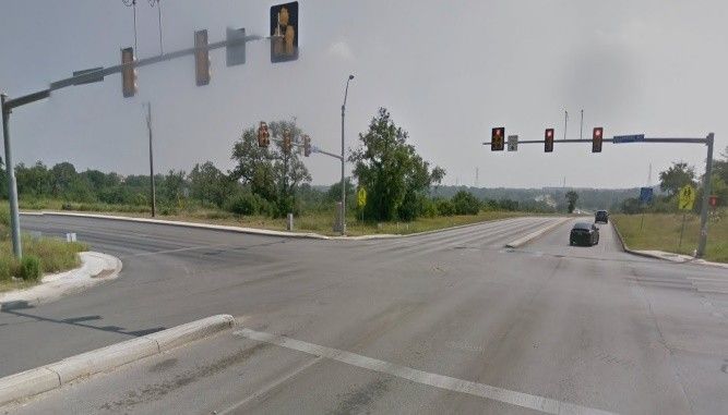 Intersection with traffic lights; vehicles on the road, with trees and a light-blue sky.