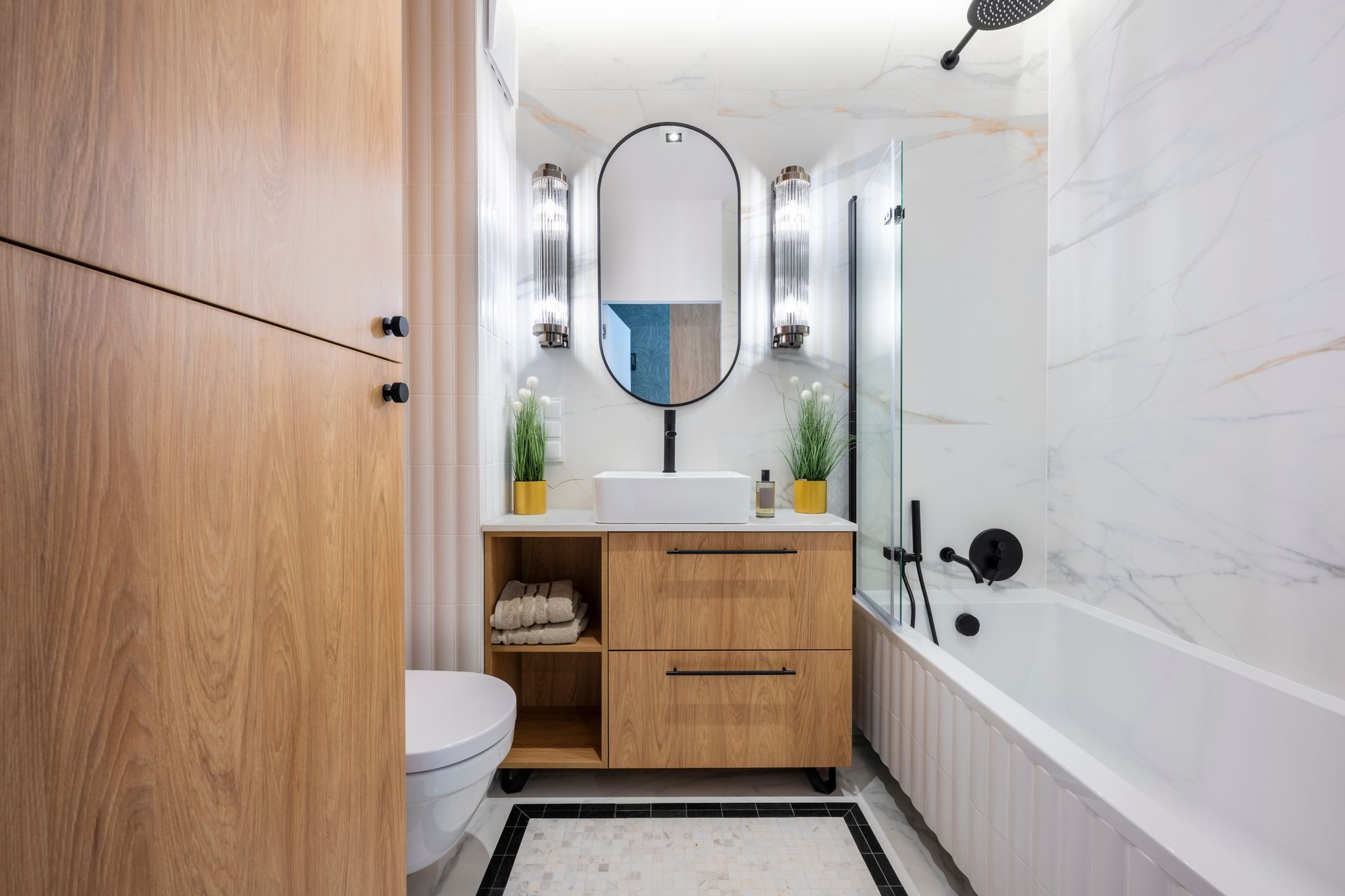 Modern bathroom with a wooden vanity, oval mirror, marble-patterned walls, and a white bathtub.