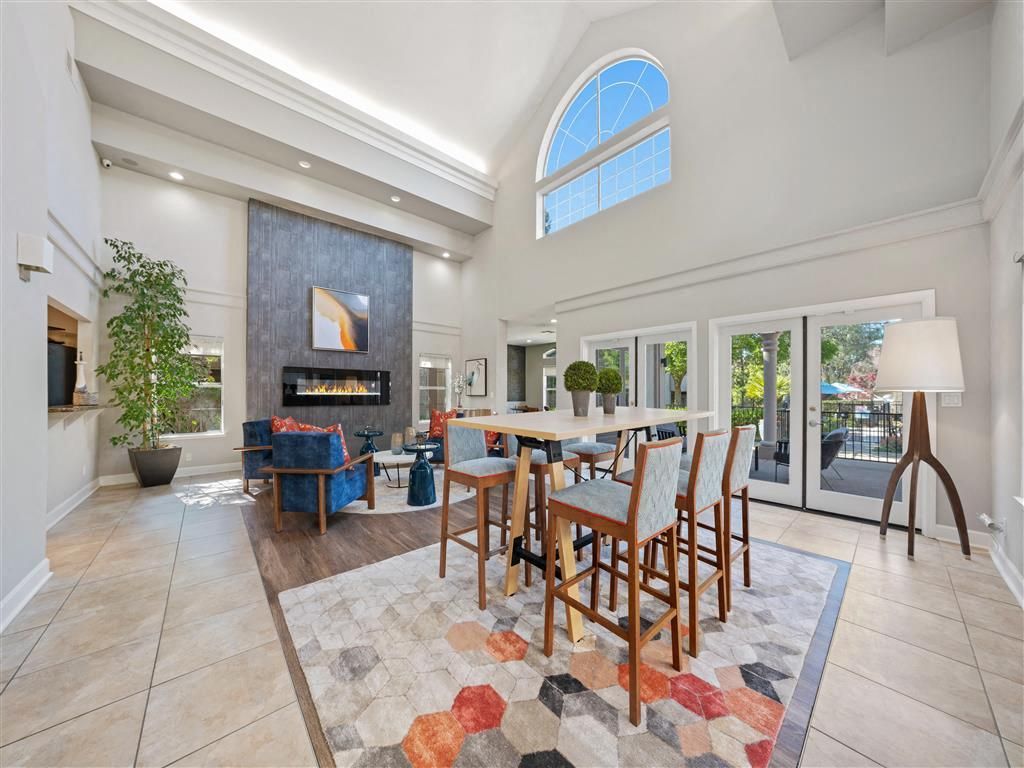 Bright two-story community lounge with a fireplace, tall arched window, and glass doors opening to an outdoor area.