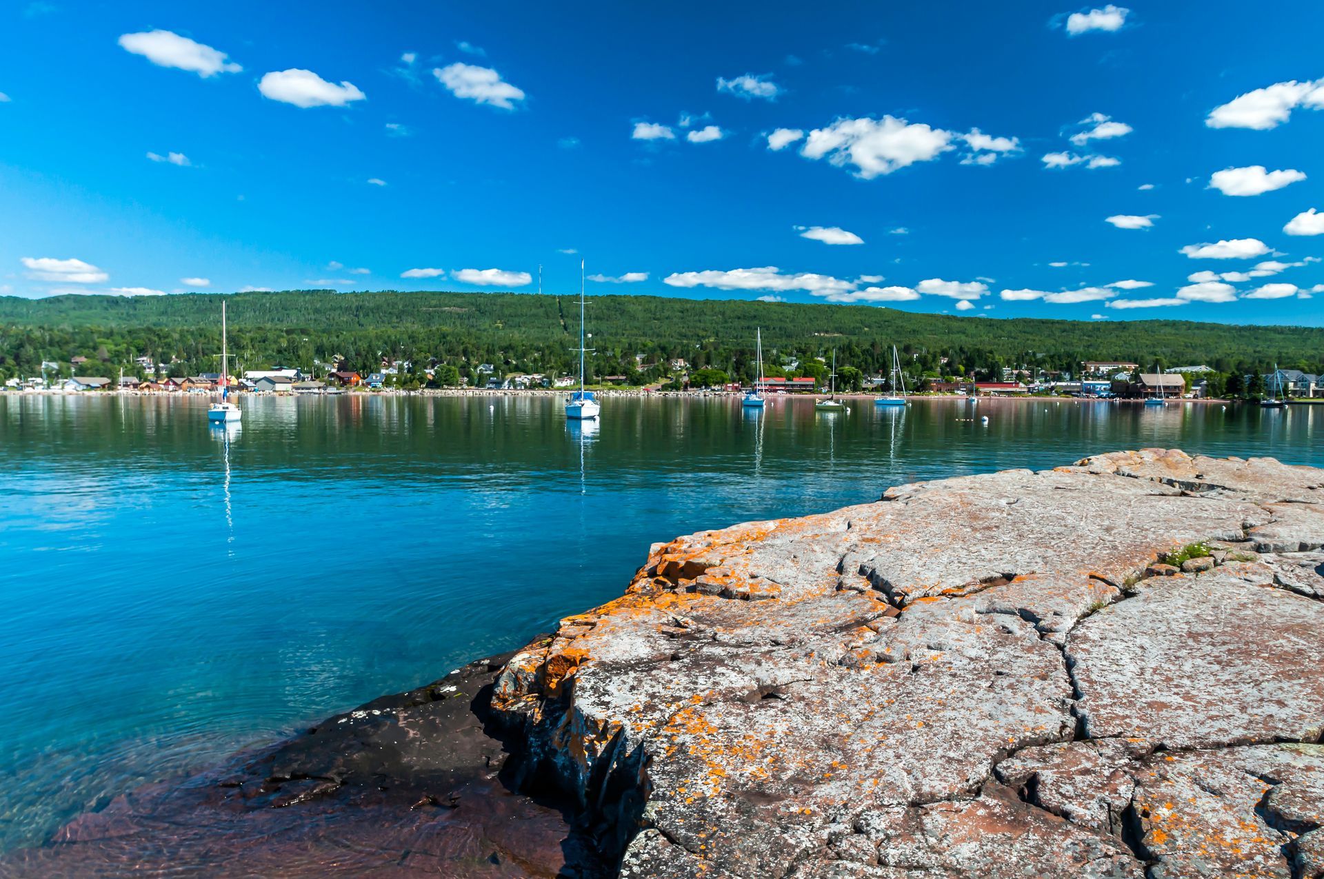 A view of a lake from a rocky shoreline with boats in the water.