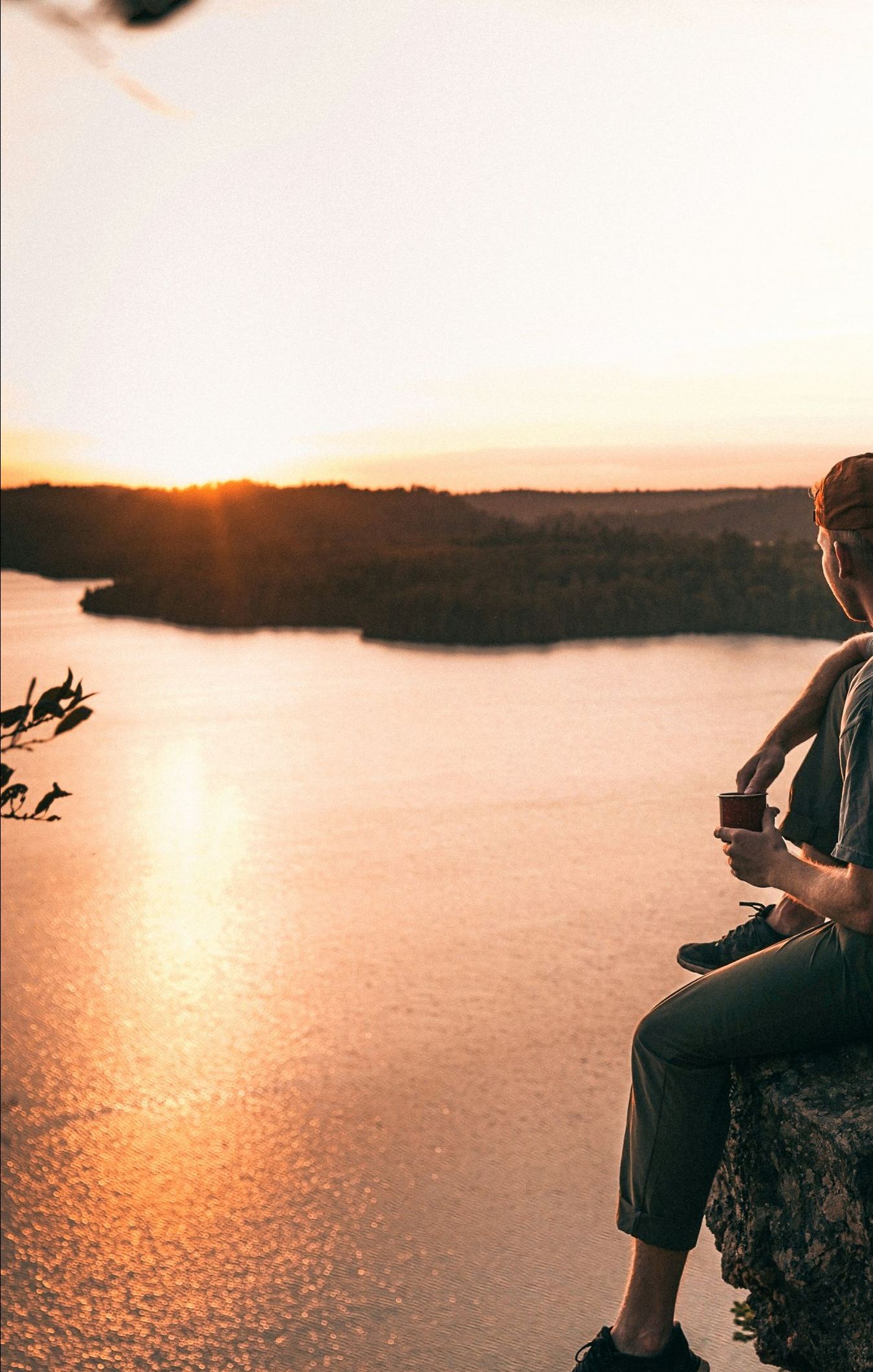 A man is sitting on a rock overlooking a lake at sunset.
