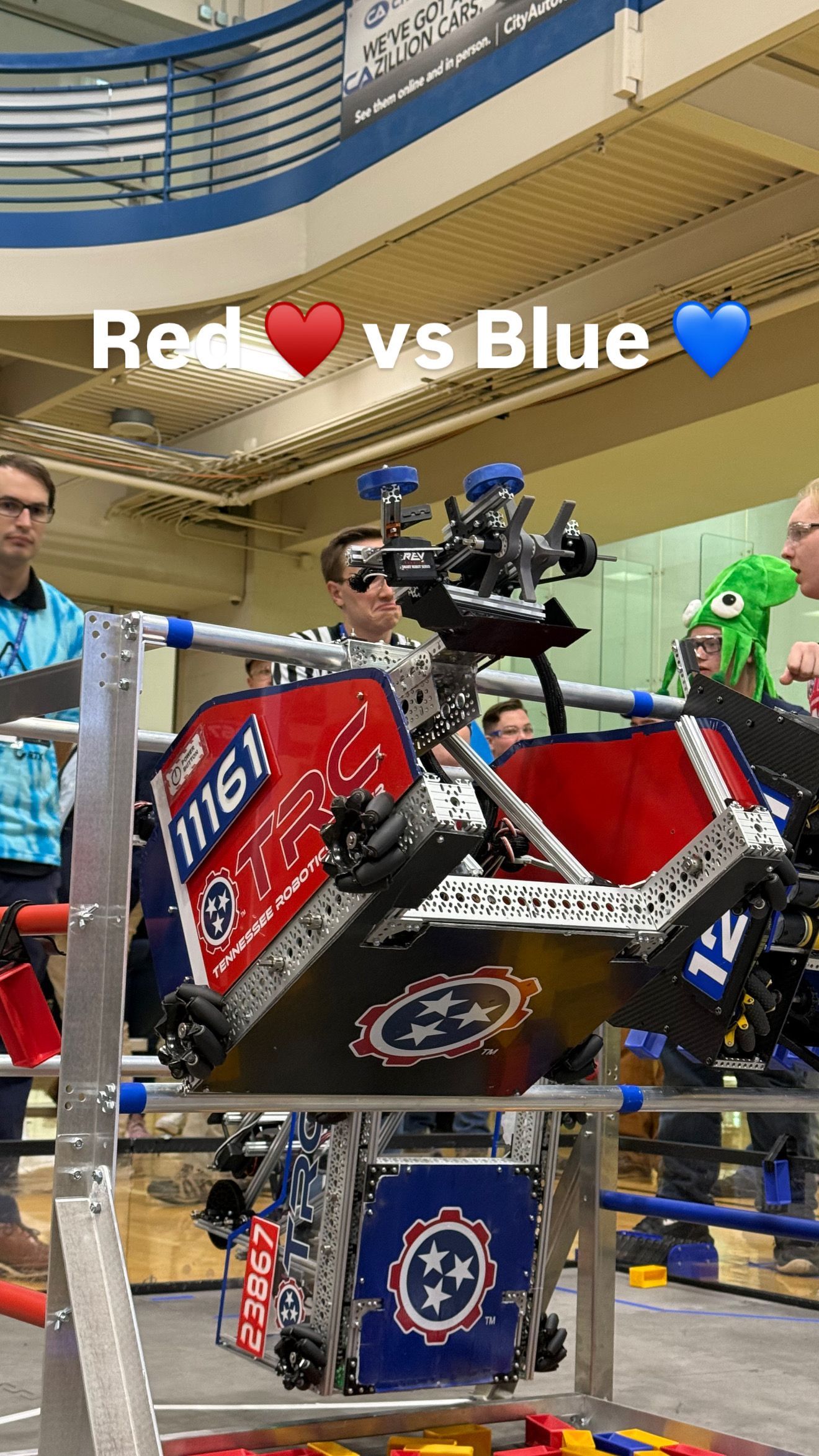 Boy smiling with a red robot decorated with the Tennessee flag. Workshop setting, American flag.