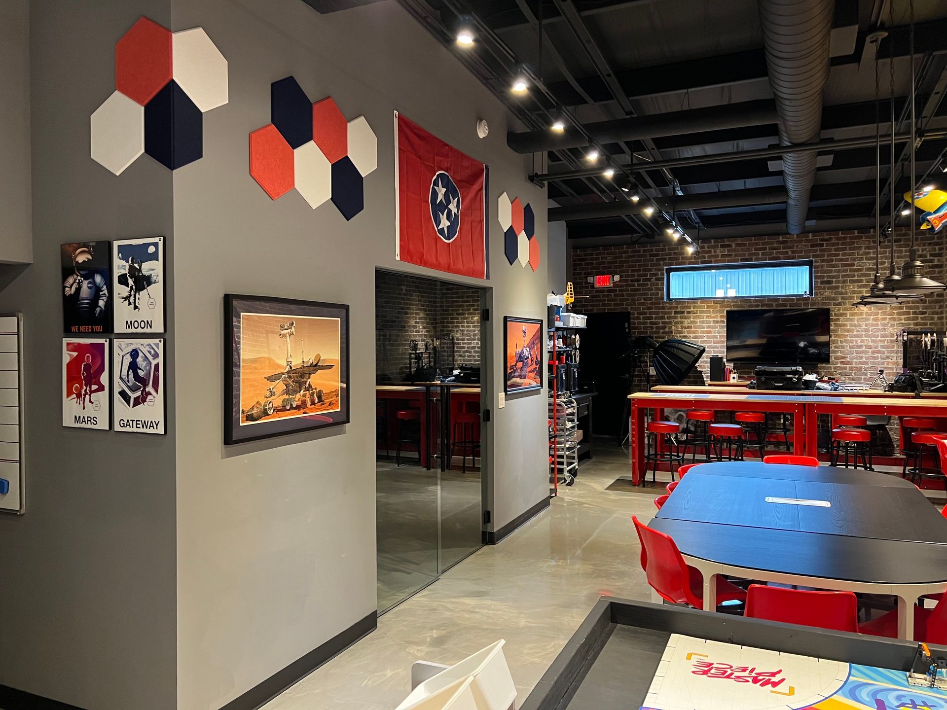 Interior of a game store with gray walls, red accents, tables, and a mirror. Hexagon art and a flag decorate a wall.
