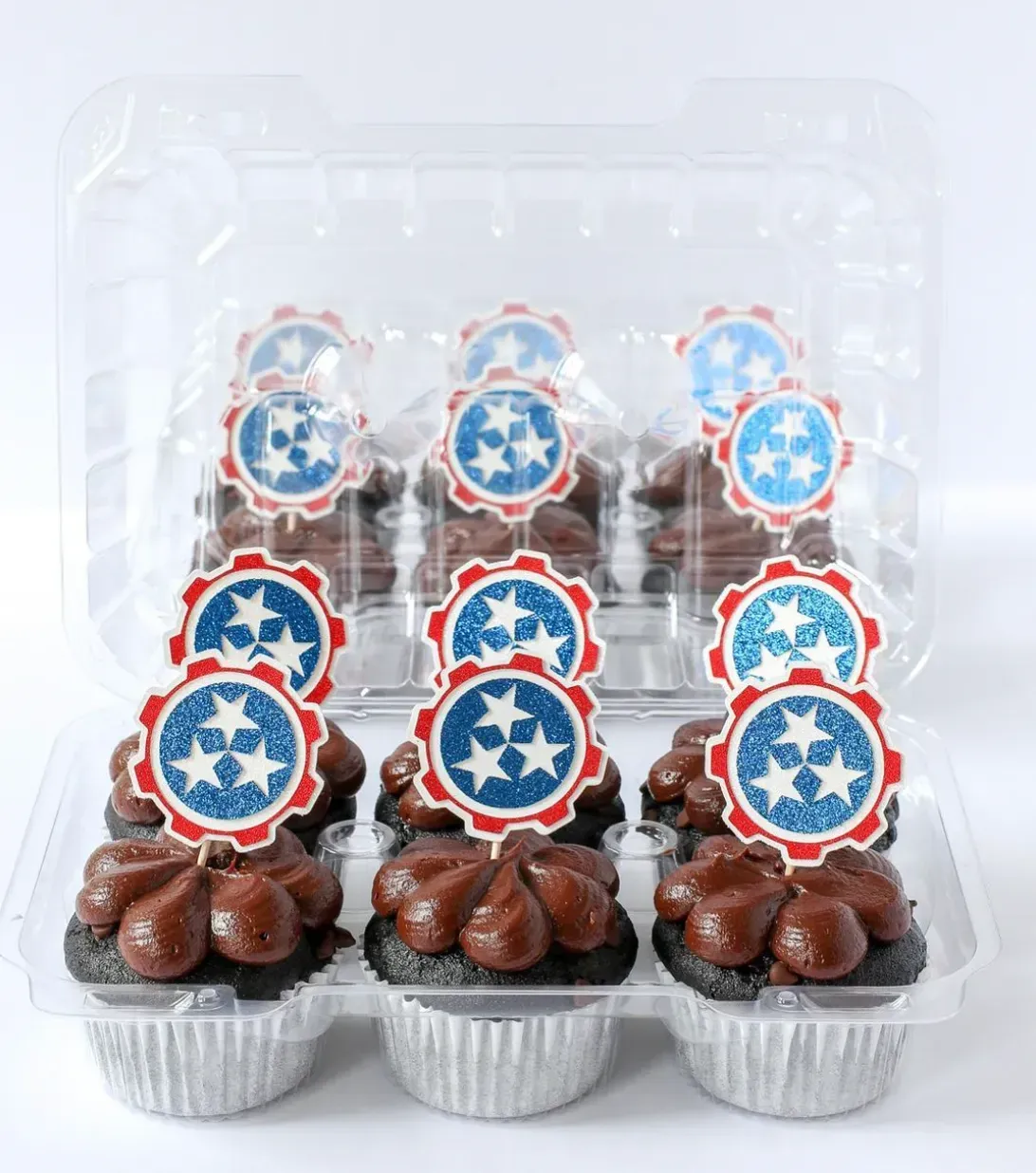 Cupcakes in a clear container with Tennessee flag toppers and chocolate frosting.