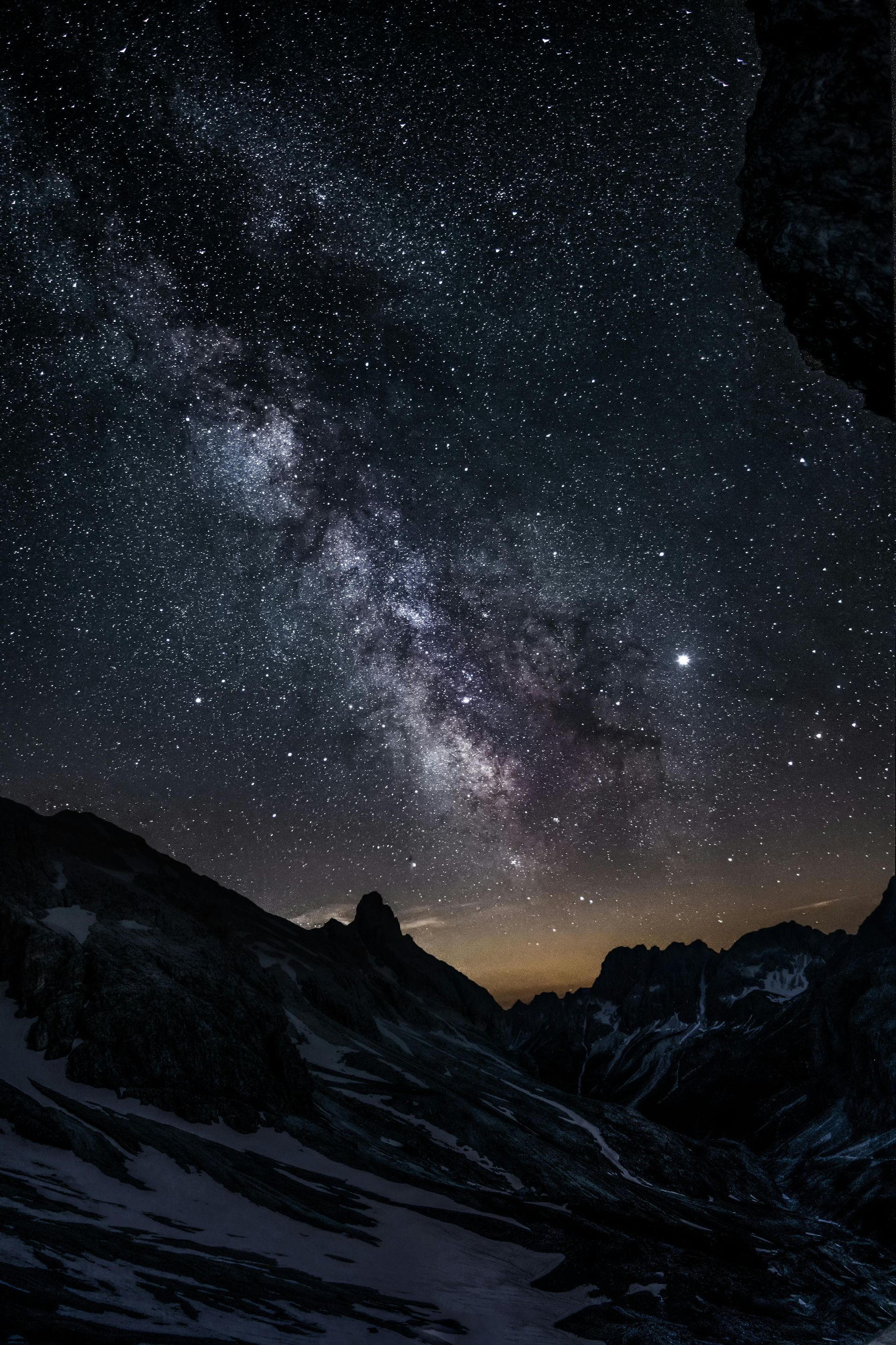 Milky Way galaxy visible above snow-covered mountains at night.