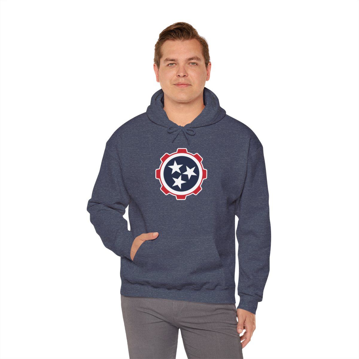 Man wearing a navy hoodie with a circular star emblem and gray pants, standing against a white background