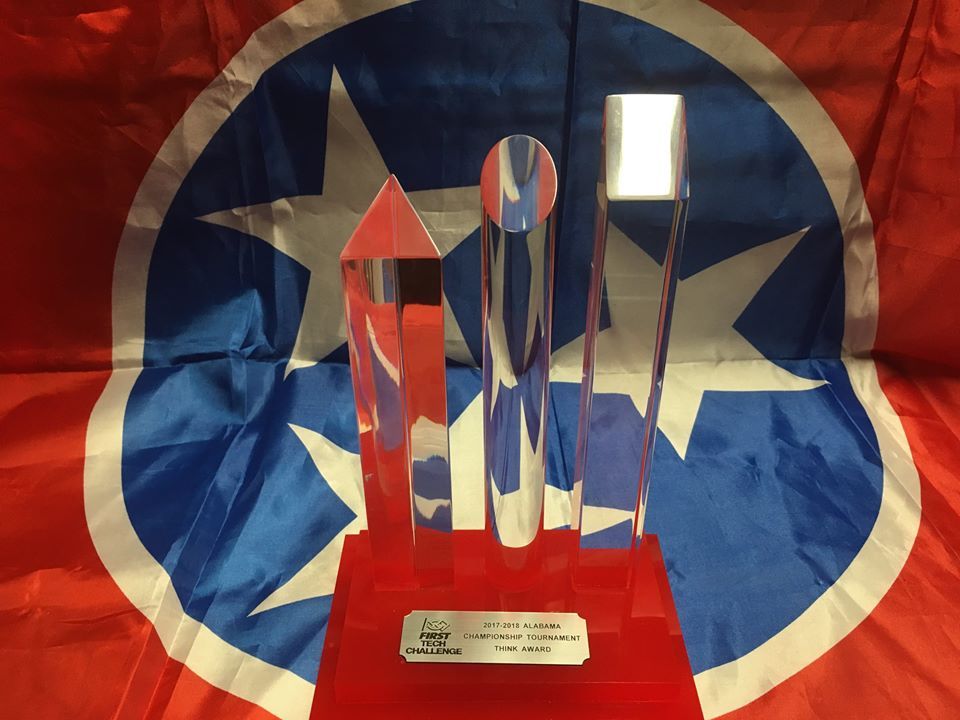 Trophy with three clear shapes on a red base in front of the Tennessee state flag.