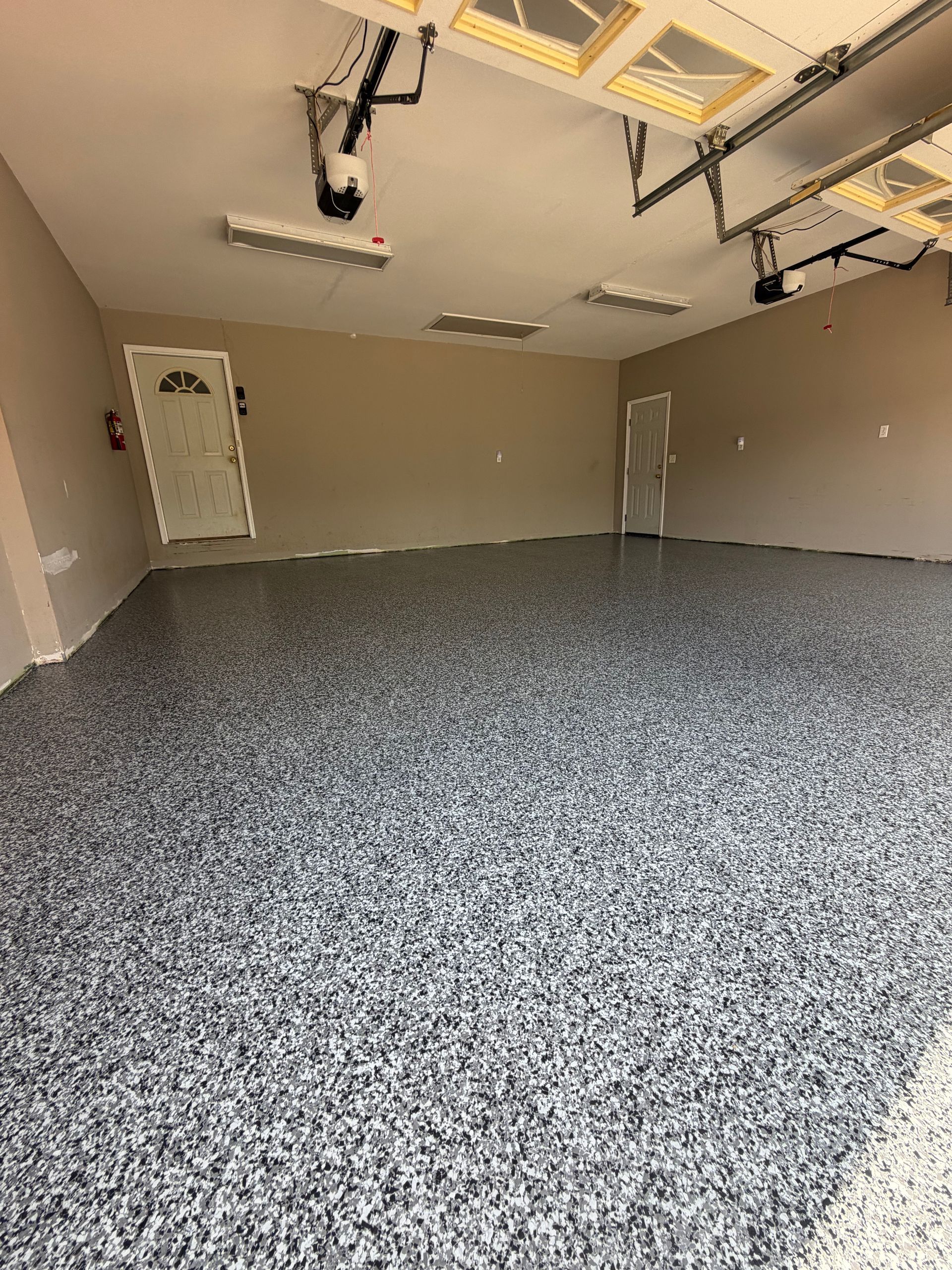 Empty garage interior with speckled epoxy floor, beige walls, and open ceiling-mounted garage door machinery