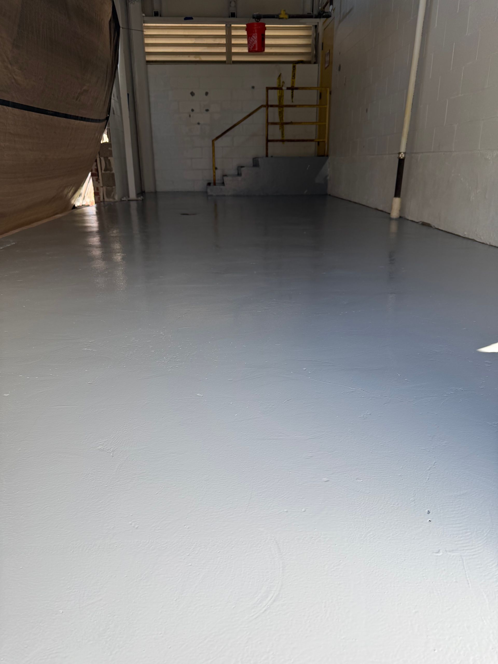A wide, empty room with light grey, smooth epoxy flooring leading to a short set of stairs at the back.