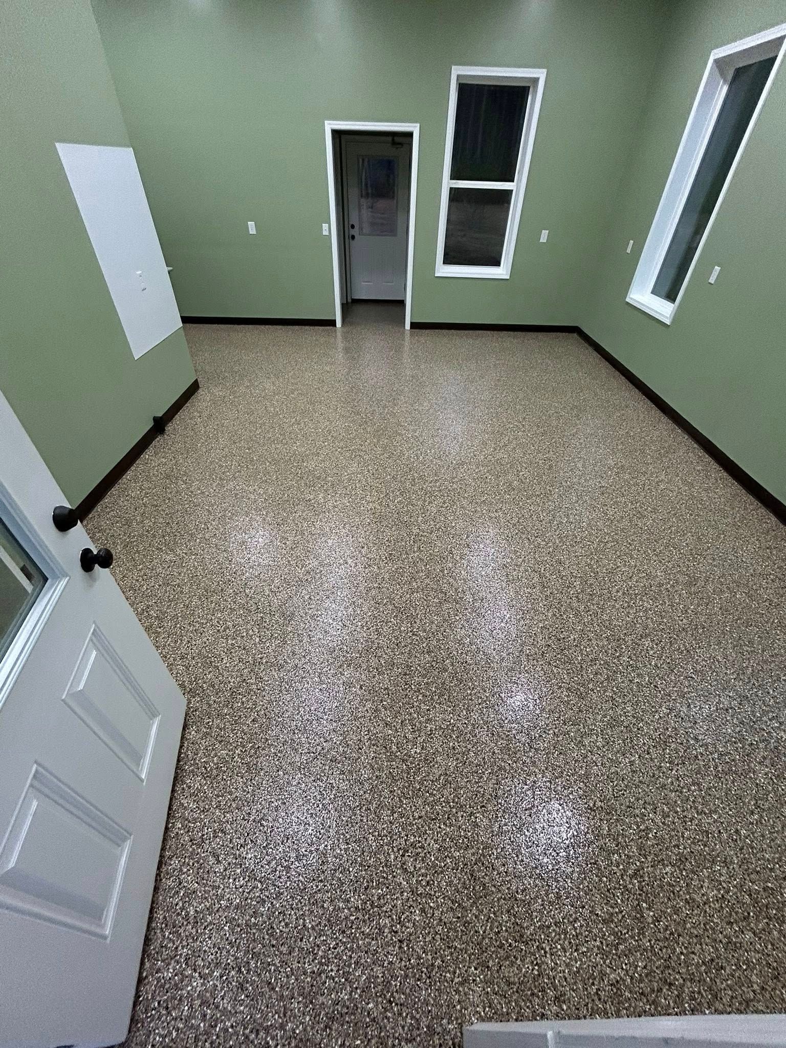Empty room with green walls, speckled floor, and a white door and windows.