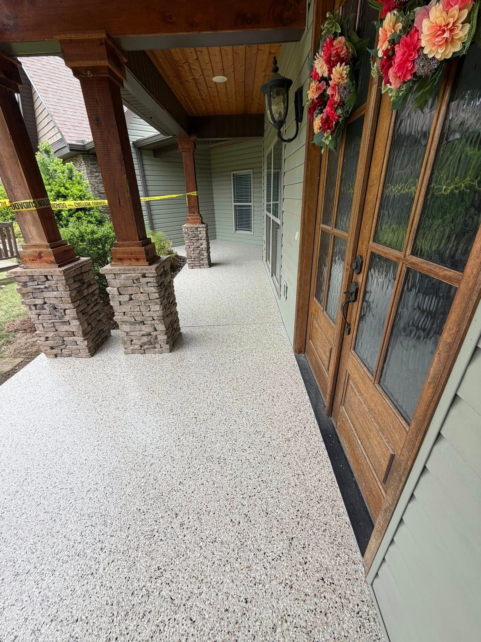 Covered front porch with stone columns, wood ceiling, flower baskets, and a glass door