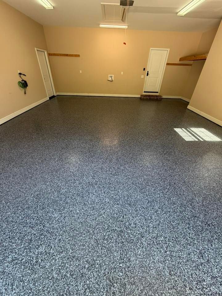 Empty garage with beige walls, speckled gray floor, overhead lights, and two white doors.