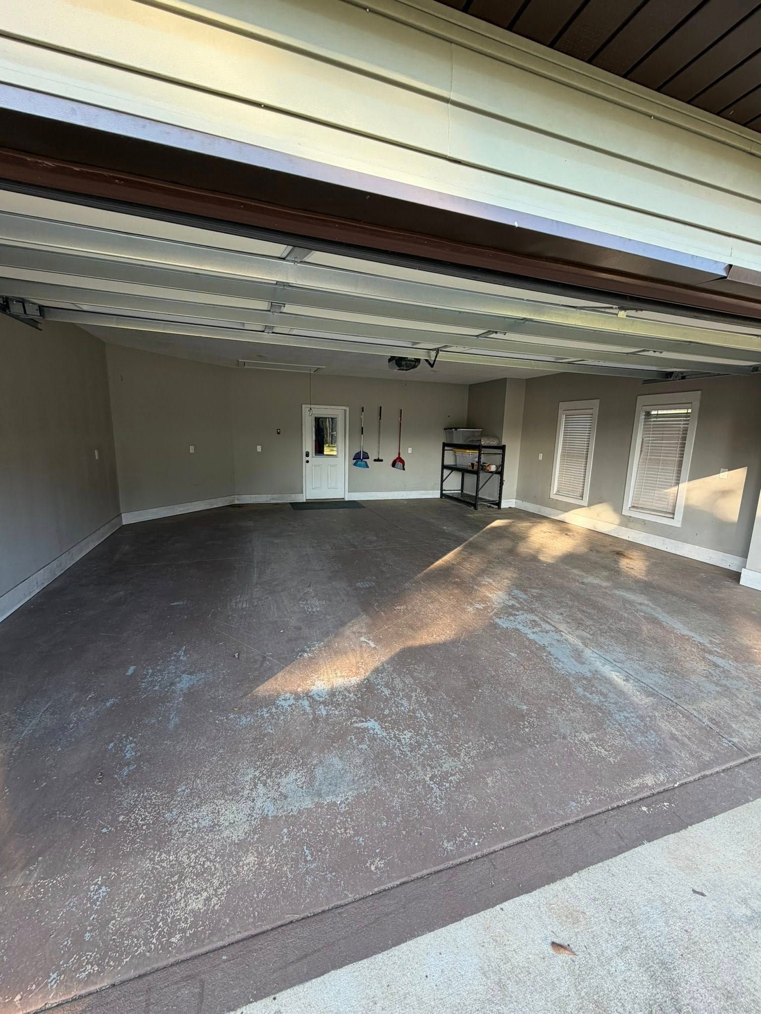 Empty garage with open door, concrete floor, and sunlight streaming in from outside.