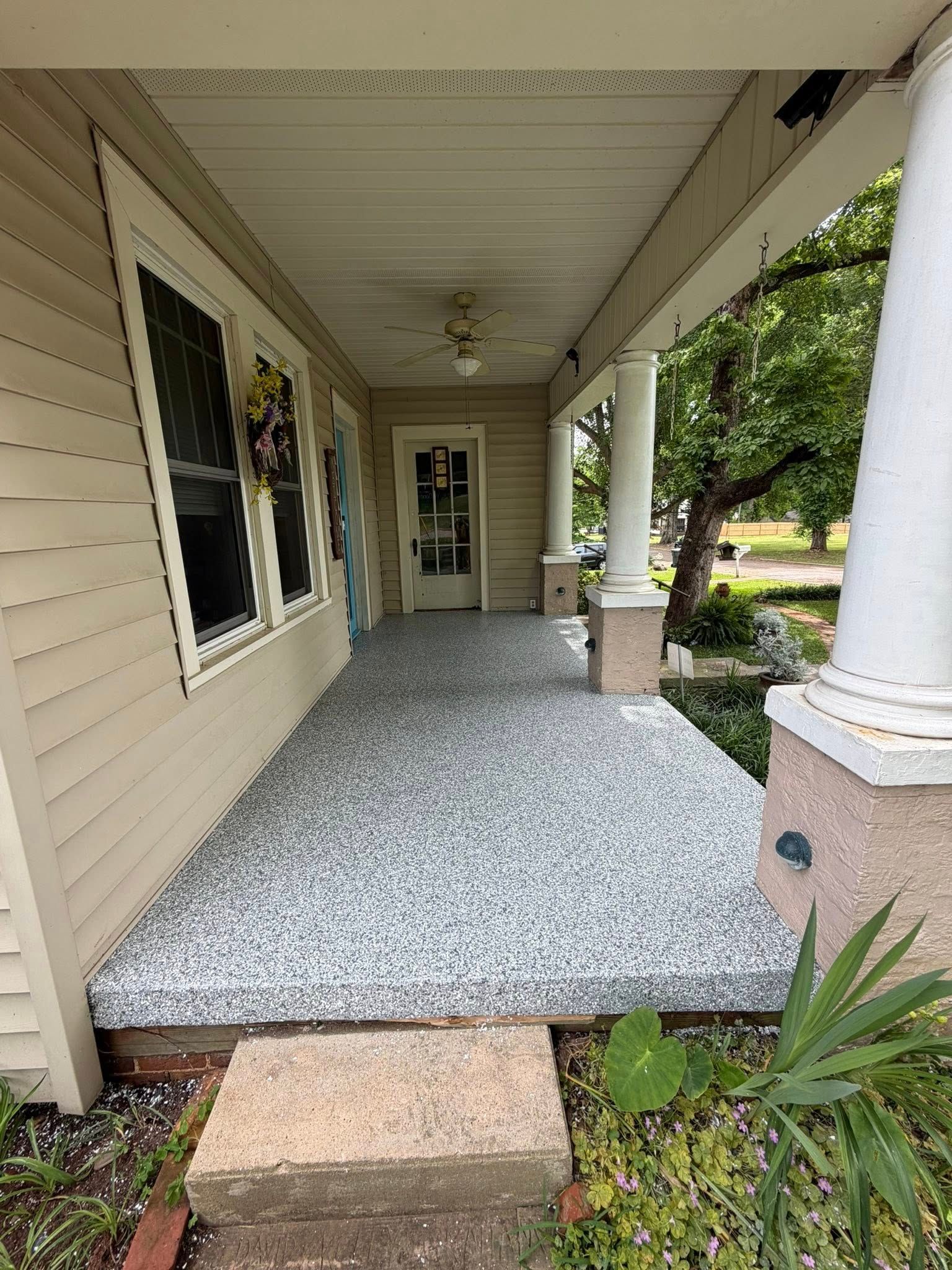 Front porch with beige siding, white columns, and a gray gravel walkway leading to the front door.