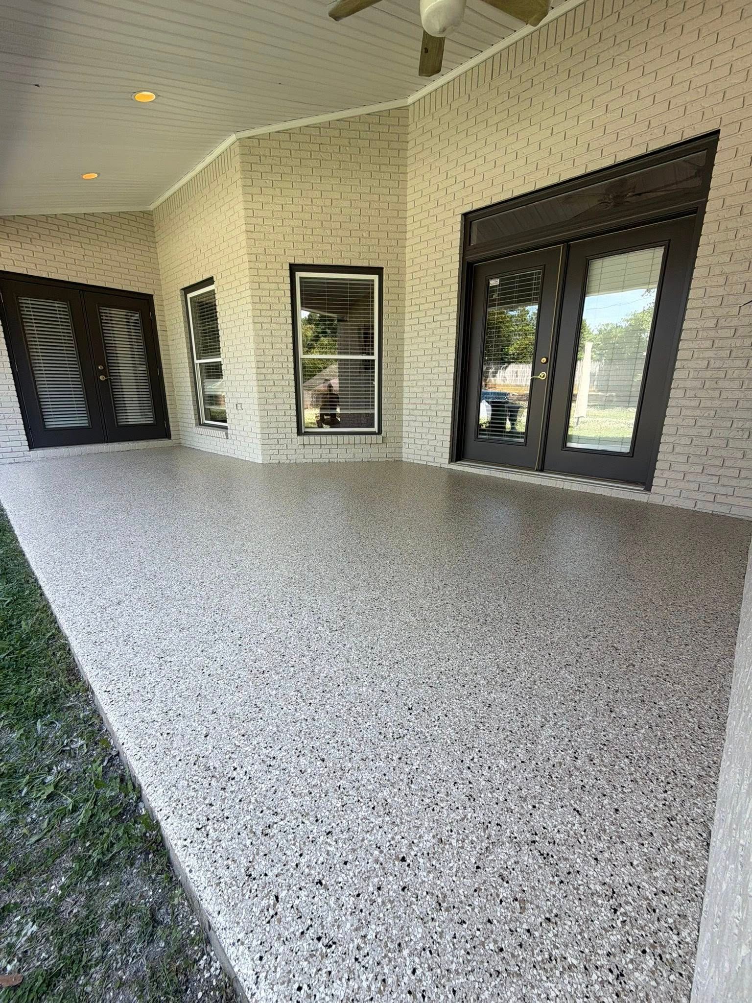 Covered patio with speckled concrete floor, tan walls, and dark-framed glass doors and windows