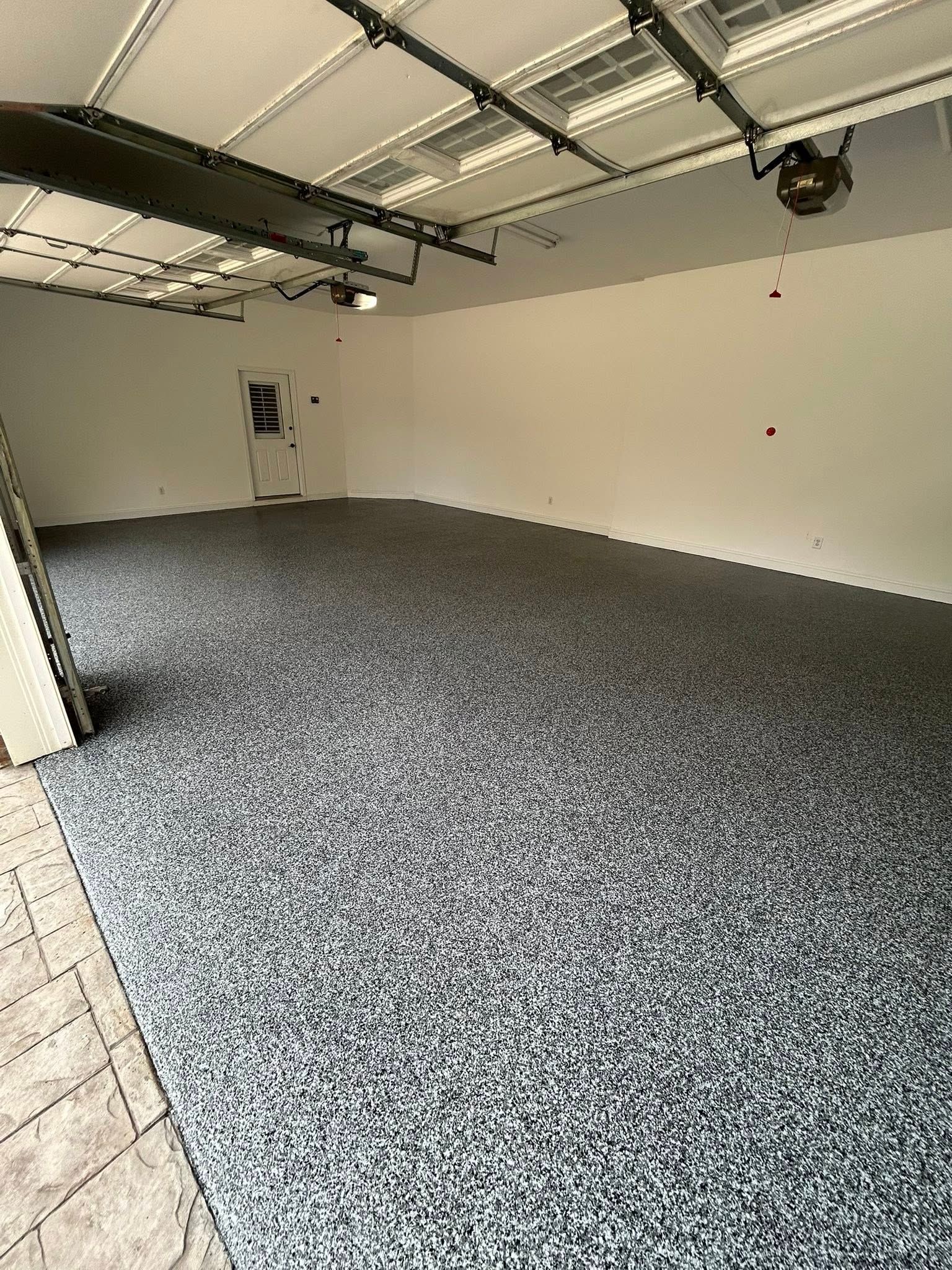 Empty garage interior with speckled epoxy floor, white walls, and overhead door tracks.