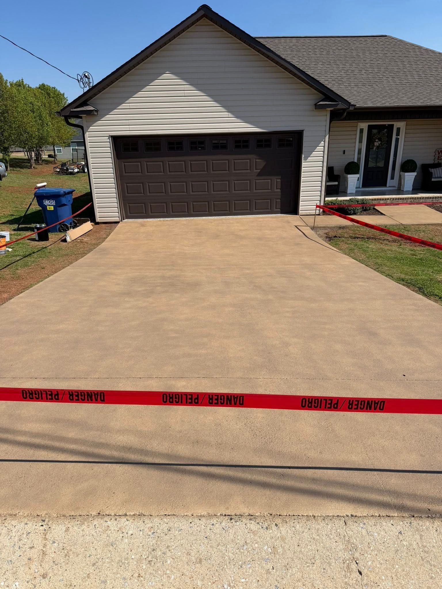 Suburban house with a two-car garage and freshly poured concrete driveway, blocked by red caution tape.