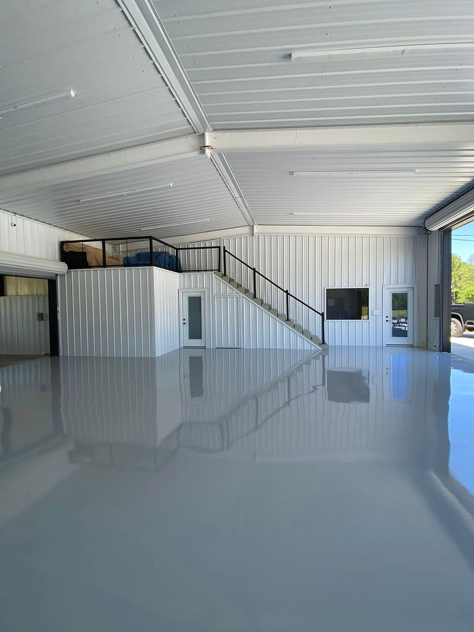 Spacious empty industrial room with glossy gray floor, corrugated metal walls, and a staircase to a loft.