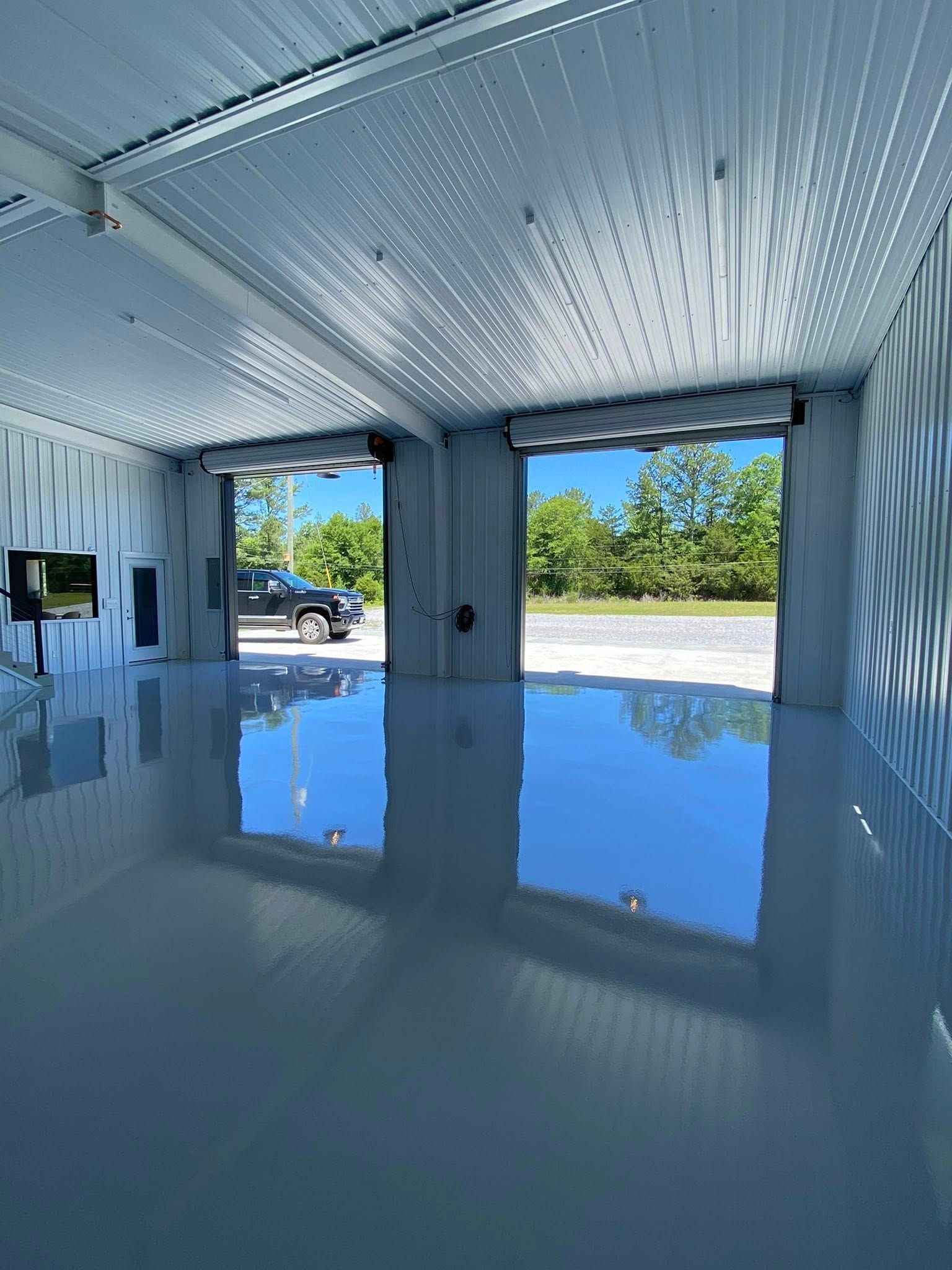 Bright empty garage with a glossy floor, corrugated metal ceiling, and open view to trees outside