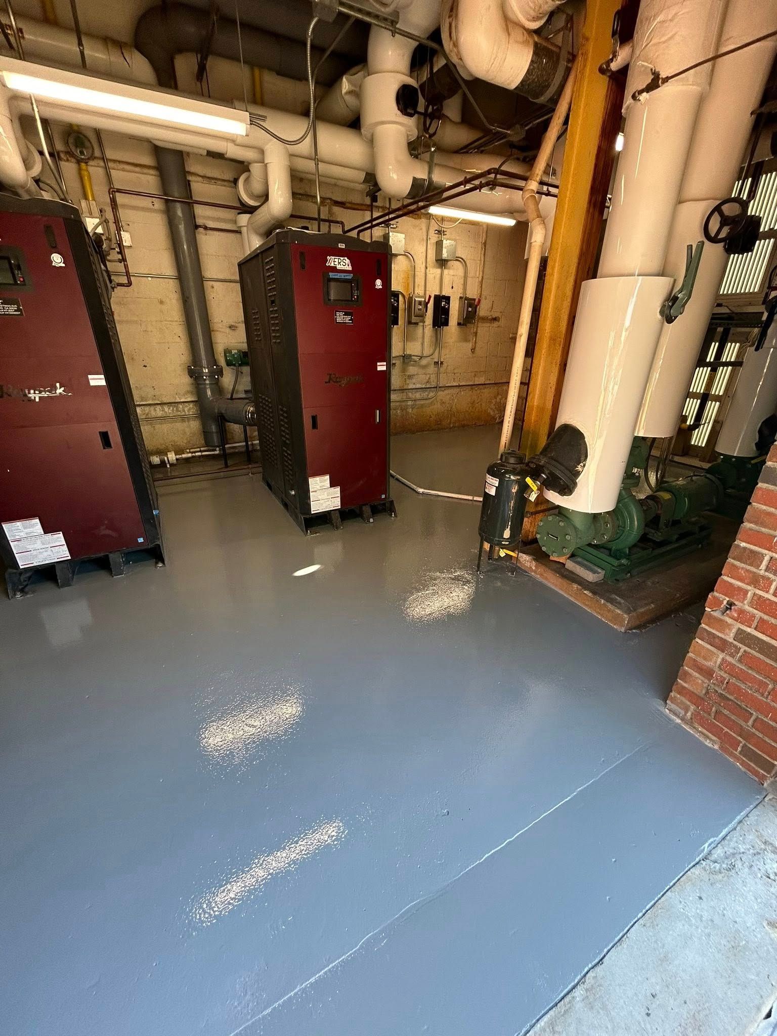 Boiler room with red equipment, exposed pipes, and a blue painted floor