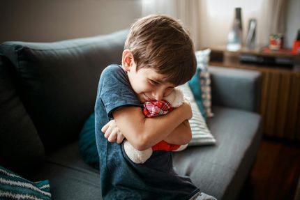 Jong kind knuffelt een rode knuffel op een grijze bank in de woonkamer.
