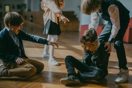 Kinderen en een volwassene hurken op een houten vloer tijdens een groepsactiviteit in een klaslokaal.