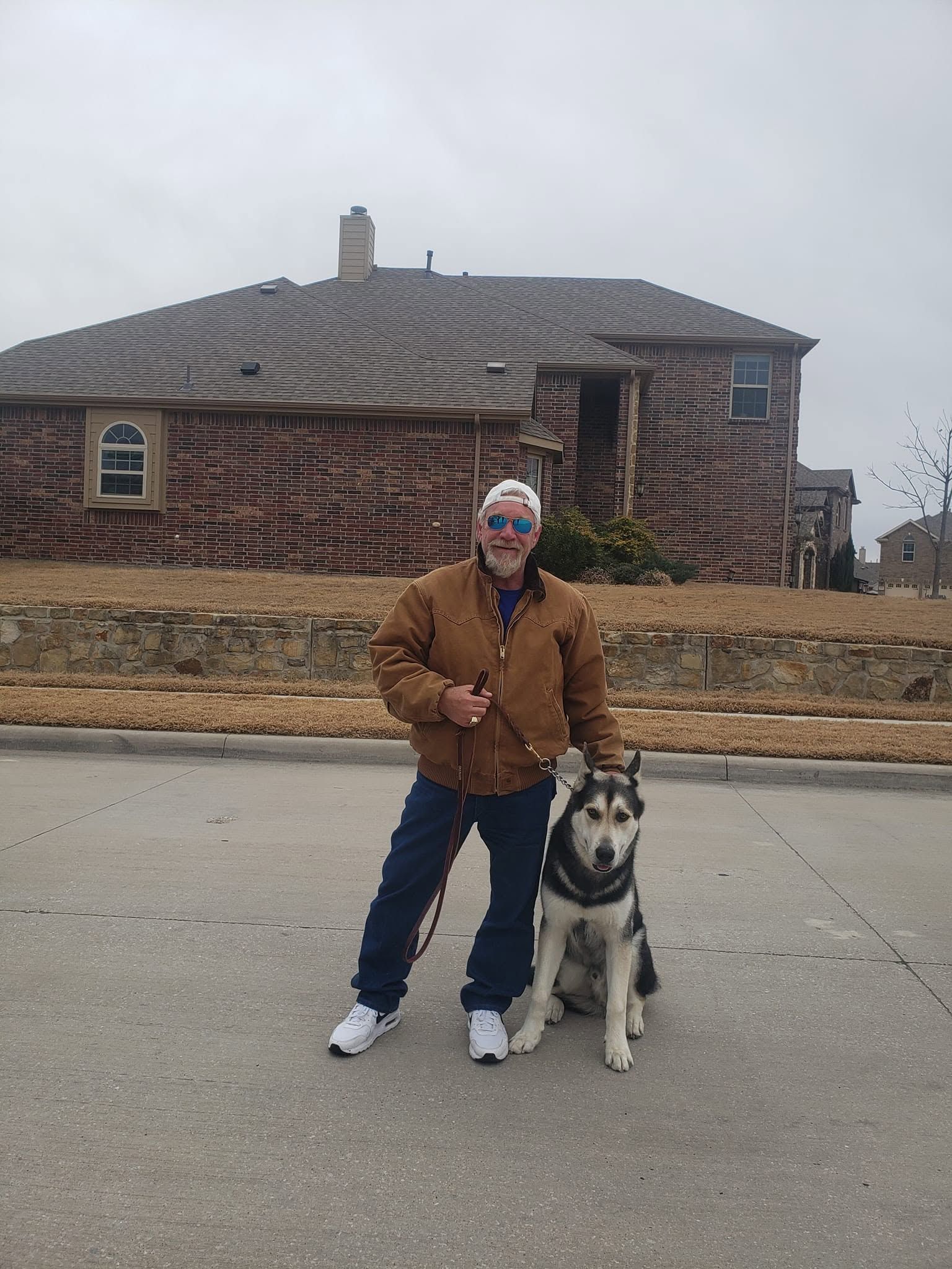 Person standing with a black-and-white dog on a street in front of a brick house