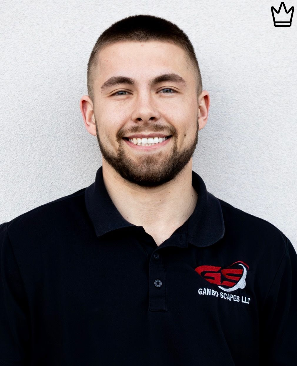 A man with a beard is wearing a black polo shirt and smiling.
