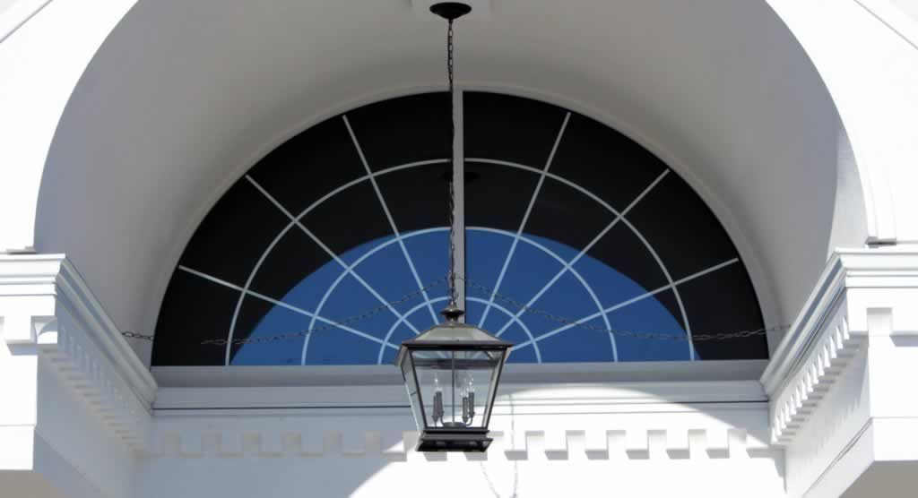 White arched window with black grid and hanging lantern above a building facade