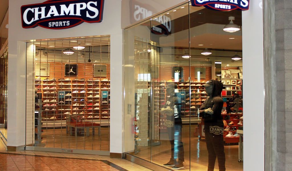 Champs Sports store entrance in a mall, with shoe displays and a person near the glass door