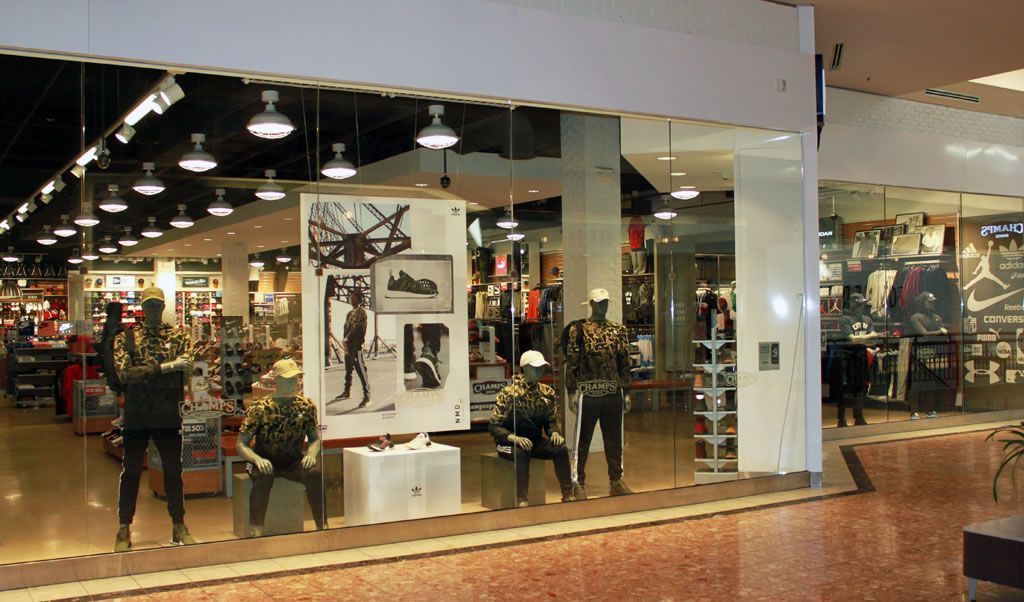 Shopping mall storefront with mannequins, clothing displays, and shoppers inside the store
