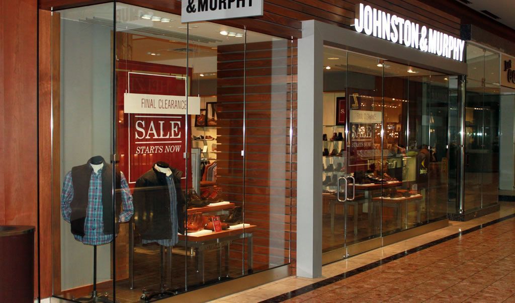 Storefront of JOHNSTON & MURPHY with a red sale sign and clothing displays inside