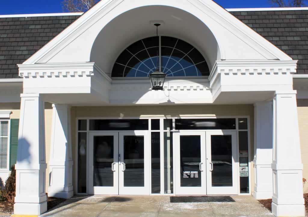 White building entrance with arched glass doors and a hanging light under a peaked portico