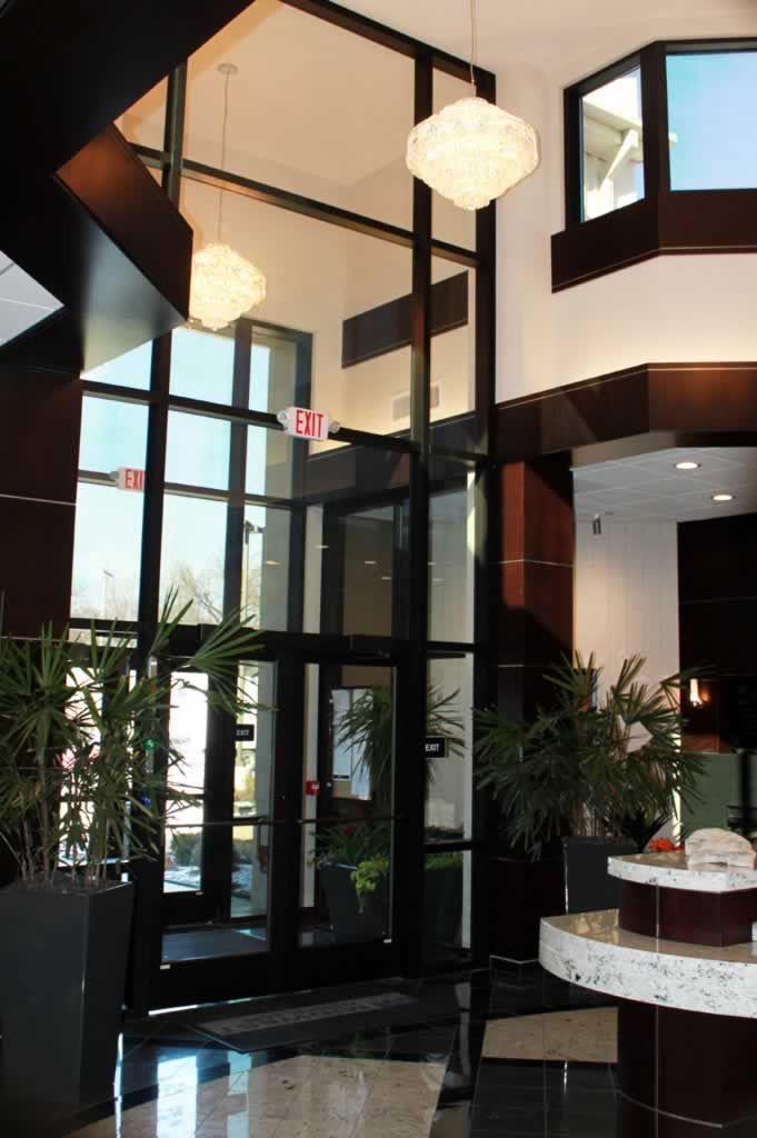 Elegant lobby with tall windows, black metal frames, hanging lights, and a small round table with flowers.