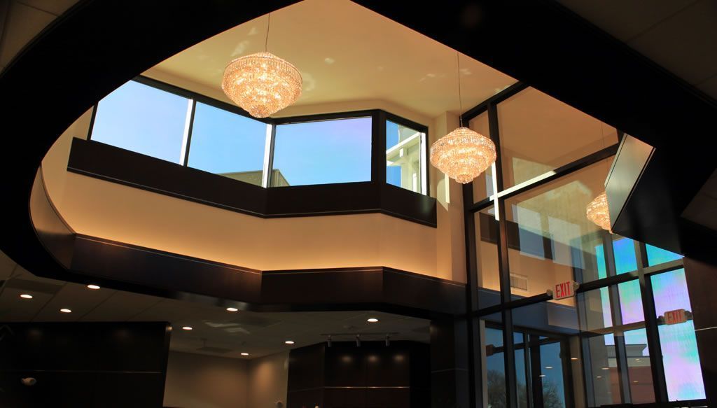 Modern lobby with hanging chandeliers, glass walls, and bright sunlight streaming in from large windows