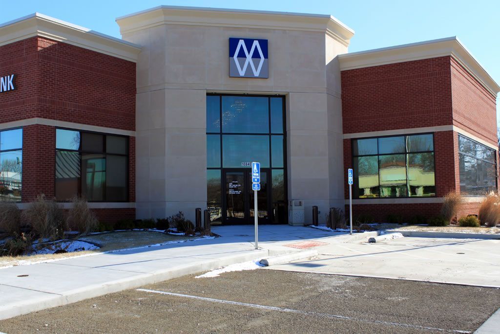 Brick-and-glass dealership building with a blue logo above the entrance and snow on the ground